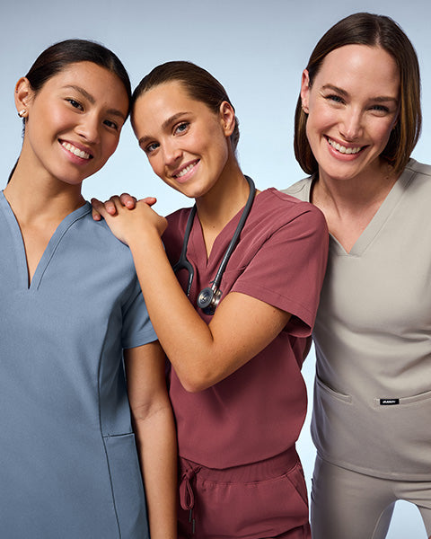 3 women wearing Storm Blue, Rosewood, and Fog color scrubs. - Women Nav Tile