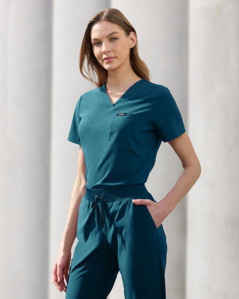 Woman wearing Carribean Blue scrubs set against a light gray background. - Women Nav Tile